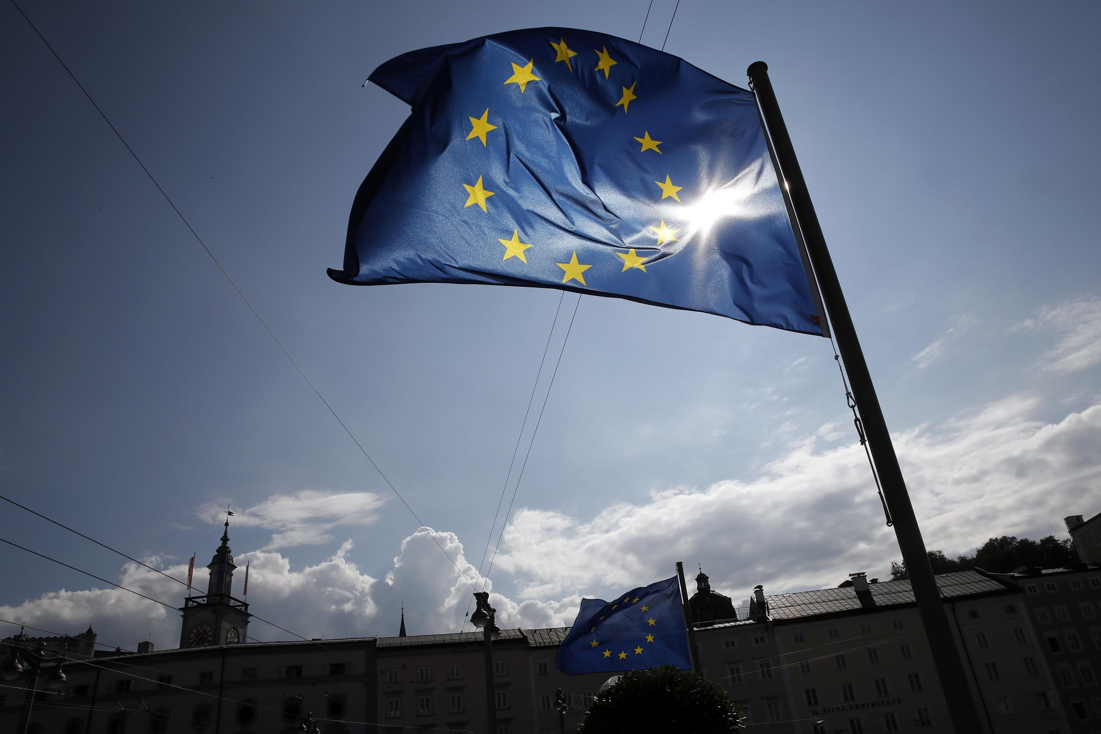 European Union flag flying on a blue sky above some buildings